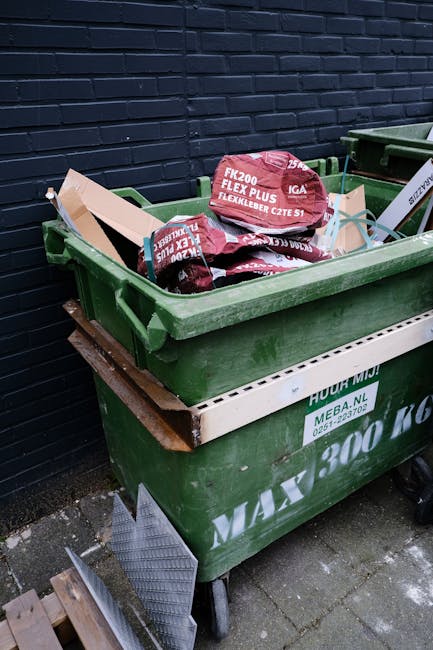 A close-up image of a pile of crumpled aluminium cans and plastic beverage containers, with some cans featuring pull-tabs and others flattened for recycling. The cans display various colours and brand